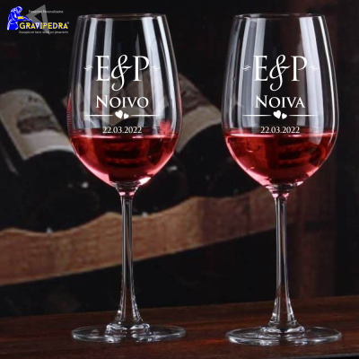 Dois copos de vinho personalizados gravados com texto branco, contendo vinho rosé, sobre mesa de madeira escura.