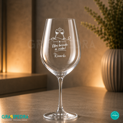 Copo de vidro para vinho gravado com texto e decoração, em mesa com fundo de parede iluminada e planta
