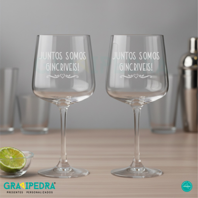 Dois copos altos de gin transparentes com texto branco em balcão de madeira clara