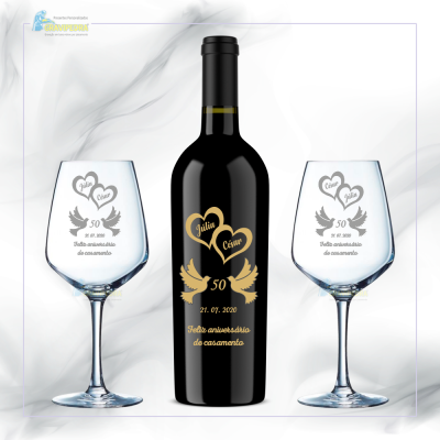 Conjunto de garrafa de vinho preta e duas taças com decoração dourada e preta de corações e texto comemorativo.