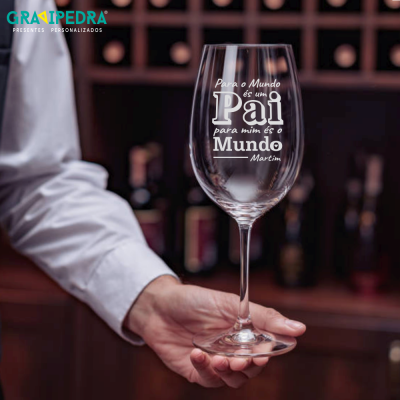 Taça de vinho com gravação personalizada segurada à frente de prateleira com garrafas
