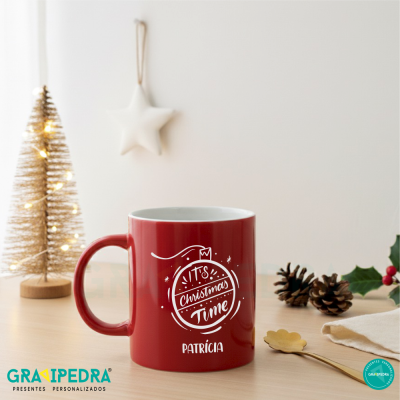 Caneca vermelha personalizada com texto de Natal sobre mesa com decoração natalícia