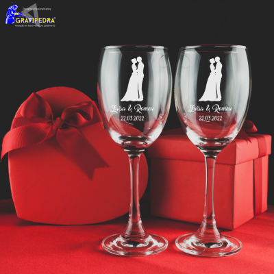 Dois copos de vidro com gravação de casal, nomes e data, com presentes vermelhos ao fundo