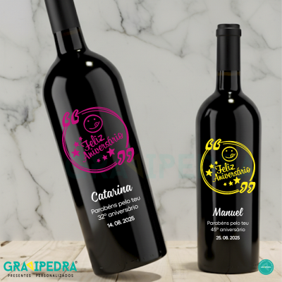 Duas garrafas de vinho personalizadas para aniversários com texto em rosa e amarelo sobre mesa de madeira e fundo marmoreado