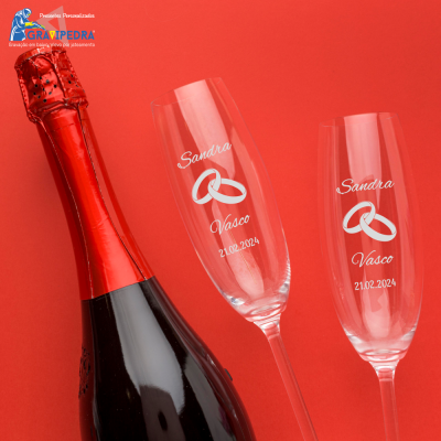 Garrafa de champanhe e duas taças gravadas com nomes, alianças e data sobre fundo vermelho.