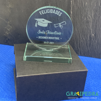 Troféu redondo de vidro transparente com inscrições em branco sobre caixa preta