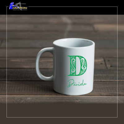 Caneca branca com letra D verde e nome Daniela, sobre mesa de madeira