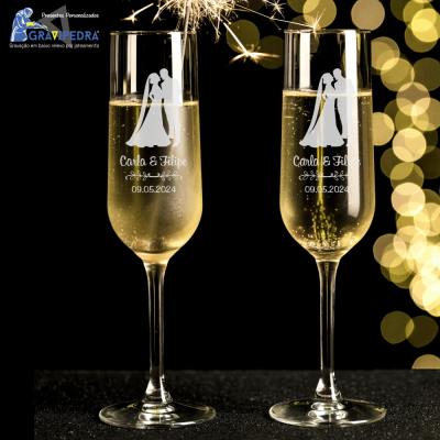 Duas taças de champanhe personalizadas com nomes e data de casamento, com fundo escuro e luzes douradas desfocadas