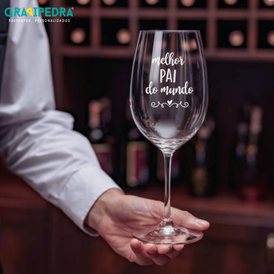 Taça de vinho com texto 'melhor PAI do mundo' segurada por uma mão em ambiente de bar.