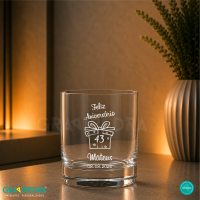 Copo de vidro com gravação de aniversário e vaso ao fundo
