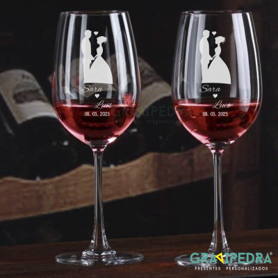Dois copos de vinho com gravuras de casal de noivos, nomes e data sobre mesa de madeira