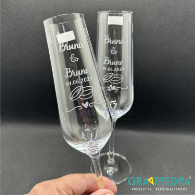 Dois copos de champanhe gravados com nomes e data, fundo preto
