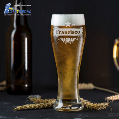 Copo de cerveja com nome 'Francisco' gravado, garrafa e espigas de trigo ao fundo