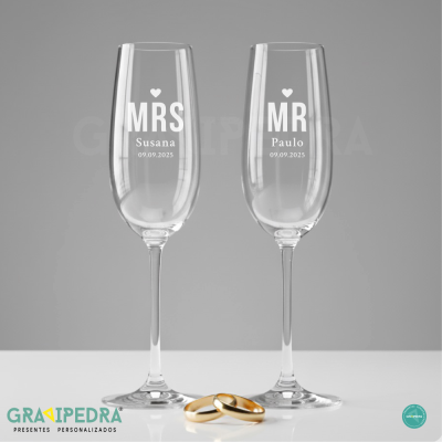 Dois copos de champanhe personalizados com nomes e data, com dois anéis dourados em frente
