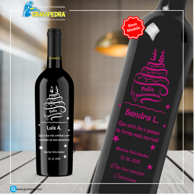 Duas garrafas de vinho personalizadas com etiquetas de aniversário, uma com texto branco e outra cor-de-rosa em vidro escuro sobre mesa de madeira.