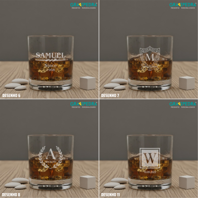 Quatro copos de whisky transparentes com diferentes gravuras brancas, sobre superfície de madeira com pequenos objetos ao lado