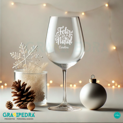 Taça de vidro com mensagem de Natal personalizada e decoração natalícia ao fundo.