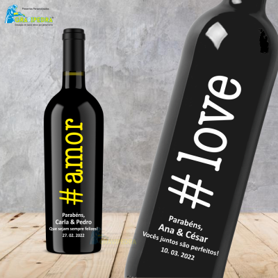 Duas garrafas pretas com textos de hashtags e felicitações em português e inglês, sobre madeira clara e fundo cinzento.