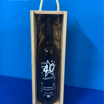 Garrafa preta comemorativa 40 aniversário em caixa de madeira com alça, fundo azul.