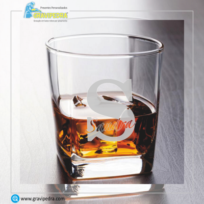 Copo de vidro com líquido cor âmbar e gravação 'Sandra'