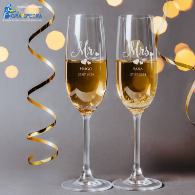 Dois copos de champagne personalizados com nomes e datas, decorados com fitas douradas