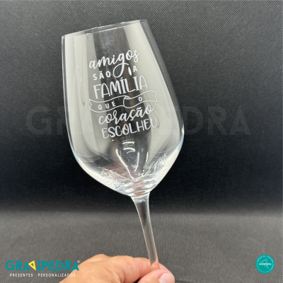 Taça de vidro com frase impressa em branco segurada por mão em fundo cinza