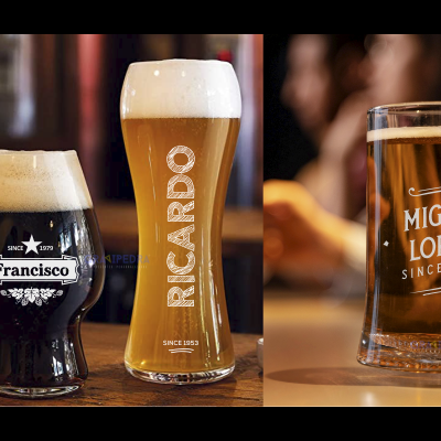 Três copos de cerveja de diferentes tipos e cores com etiquetas personalizadas, sobre uma mesa de madeira.