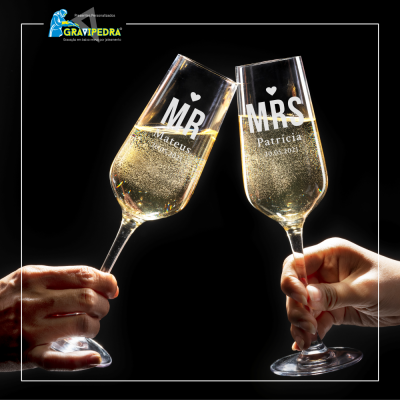 Duas taças de champanhe personalizadas com texto, seguradas por mãos sobre fundo preto