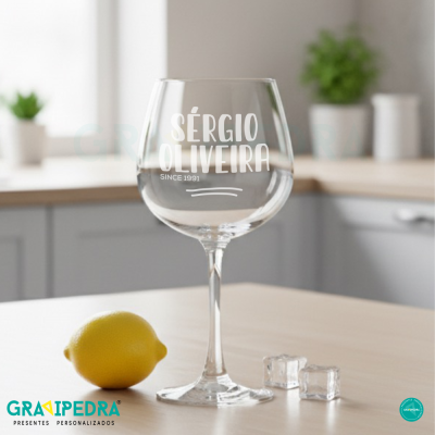 Copo de vinho transparente com texto branco ao lado de limão e cubos de gelo numa mesa clara