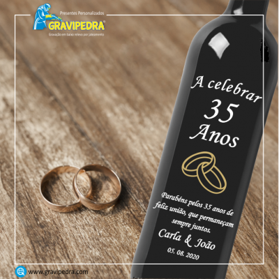 Garrafa preta comemorativa de 35 anos com texto gravado e dois anéis dourados ao lado sobre mesa de madeira.