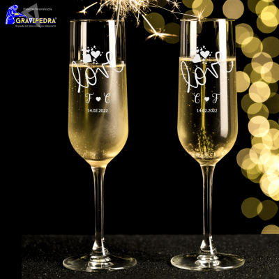 Duas taças de champanhe gravadas com texto e corações em fundo escuro com luzes douradas
