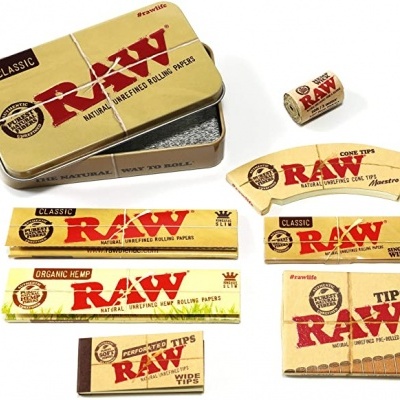 Conjunto de acessórios para tabaco da marca RAW com embalagens amarelas e castanhas e caixa metálica.