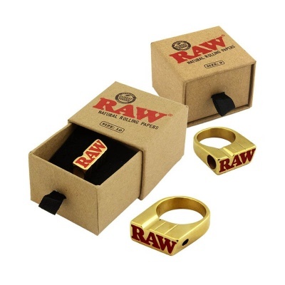 Anel dourado com inscrição RAW em caixa de papelão