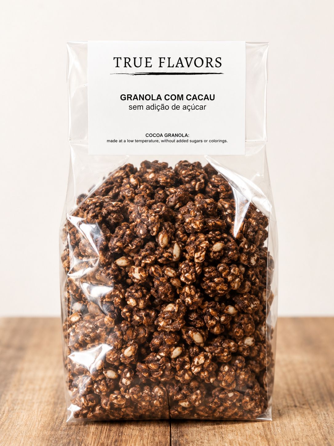 True Colors Granola com Cacau Pacote transparente de granola com cacau, etiqueta branca com texto True Flavors, sobre mesa de madeira clara