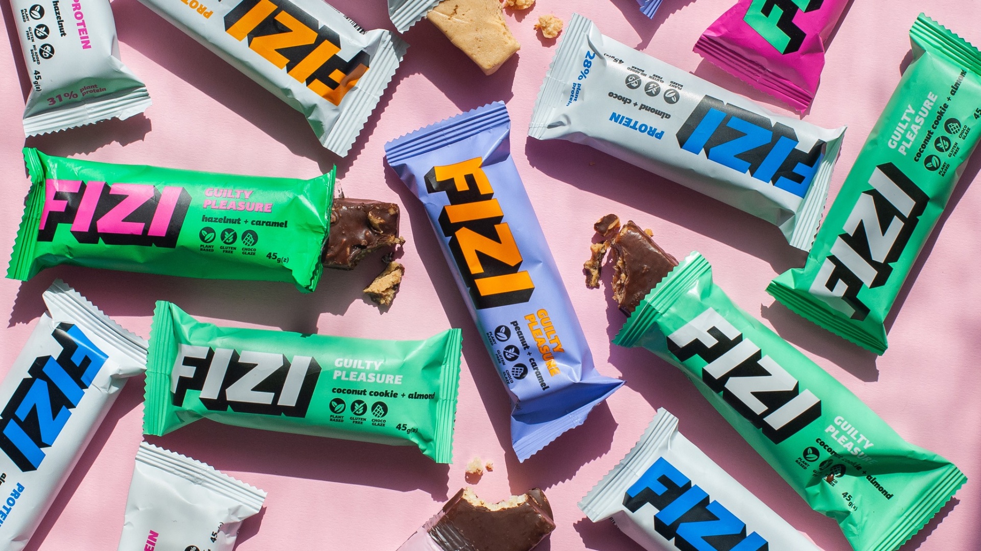 Barrinha Guilty Pleasure Barritas energéticas em várias embalagens coloridas sobre fundo rosa.