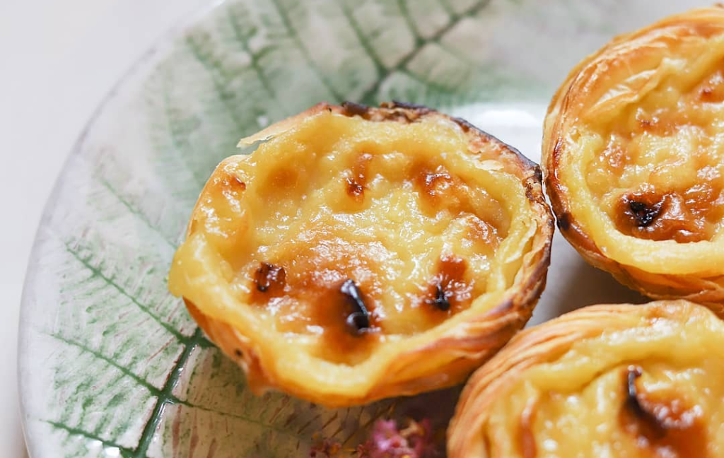 Três pastéis de nata em prato com padrão de folhas verdes