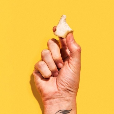 Mão segurando pedaço pequeno de pão contra fundo amarelo