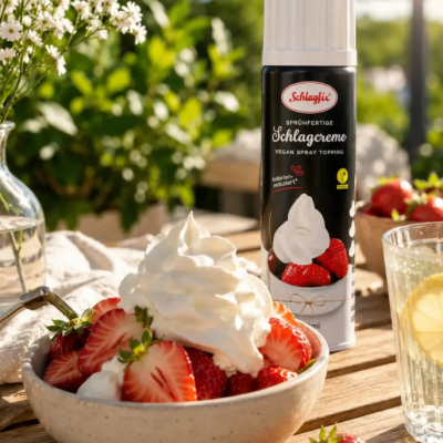 Spray chantilly vegan Schlagfix ao lado de taça com morangos e chantilly numa mesa ao ar livre