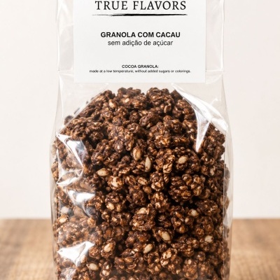 Pacote transparente de granola com cacau, etiqueta branca com texto True Flavors, sobre mesa de madeira clara