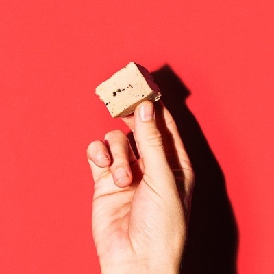 Mão segurando cubo bege com manchas escuras sobre fundo vermelho