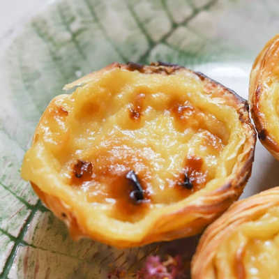 Três pastéis de nata em prato com padrão de folhas verdes