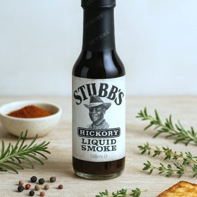 Garrafa de Stubb's Hickory Liquid Smoke em superfície com ervas e especiarias
