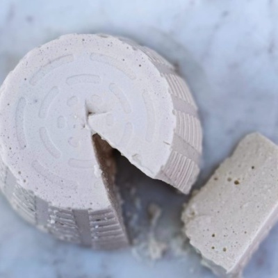 Queijo fresco branco com textura granulada cortado em fatia sobre mármore branco