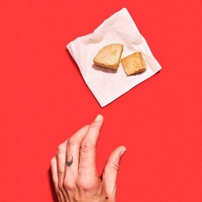 Mão com tatuagem a tentar alcançar duas fatias de pão torrado sobre guardanapo branco em fundo vermelho