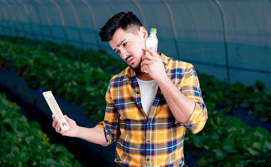 Homem de camisa xadrez com garrafa e régua numa estufa agrícola