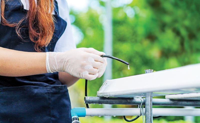 Pessoa com luvas a manipular equipamento metálico branco com tubo preto