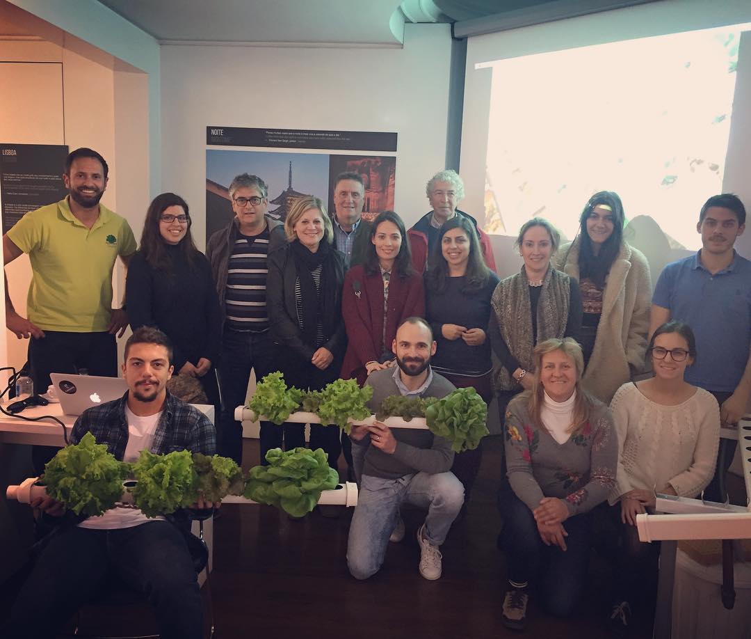 Grupo de pessoas segurando hortaliças verdes em sala com posters e projetor