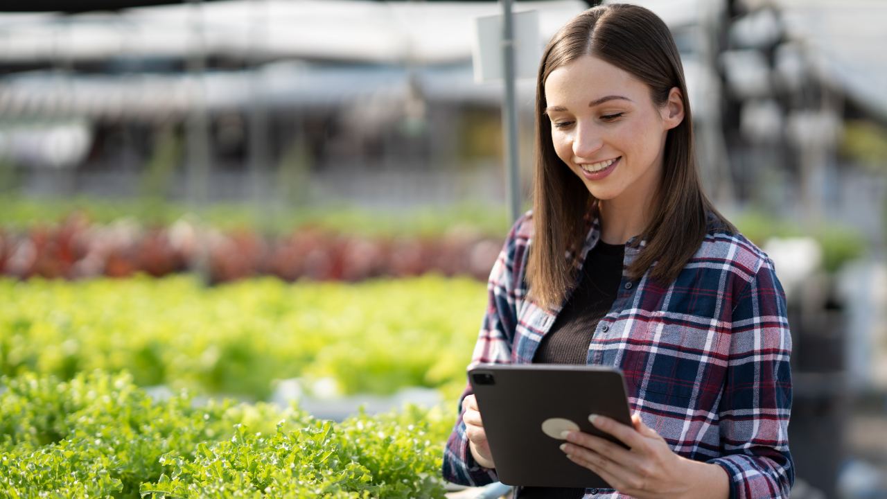 Mulher jovem com camisa xadrez segurando tablet em estufa com plantas verdes