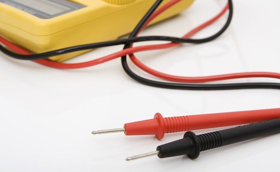Multímetro digital amarelo com sondas vermelha e preta sobre fundo branco