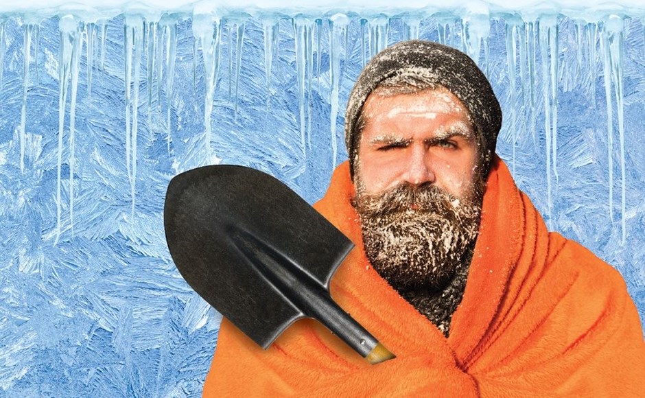 Homem com gorro cinzento e manta laranja segurando uma pá preta em ambiente gelado